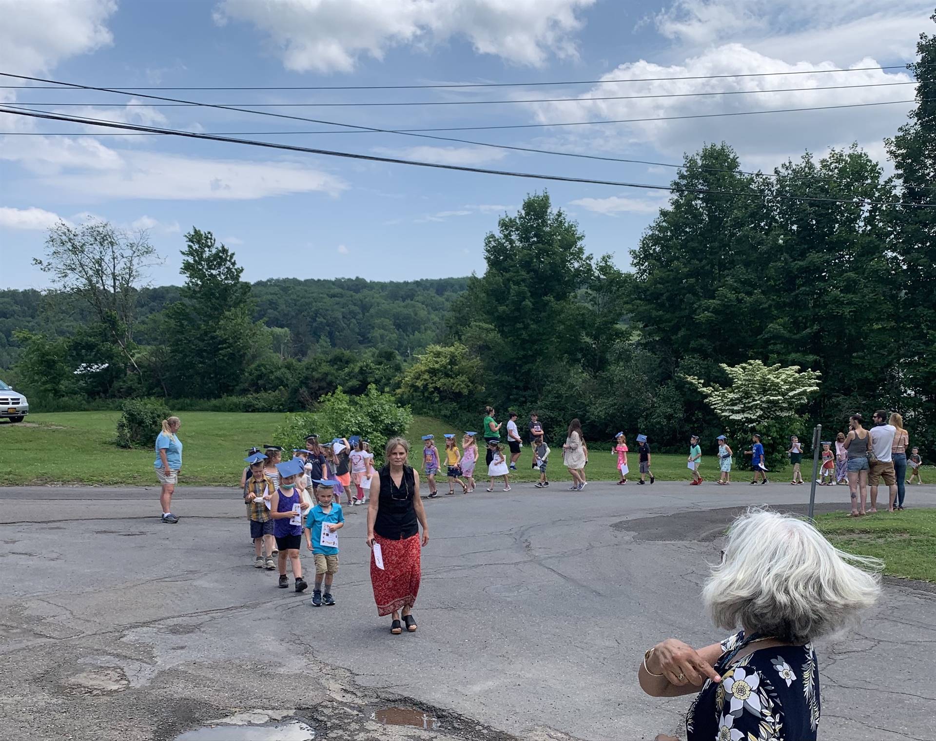 students parade on a driveway with trees in background.