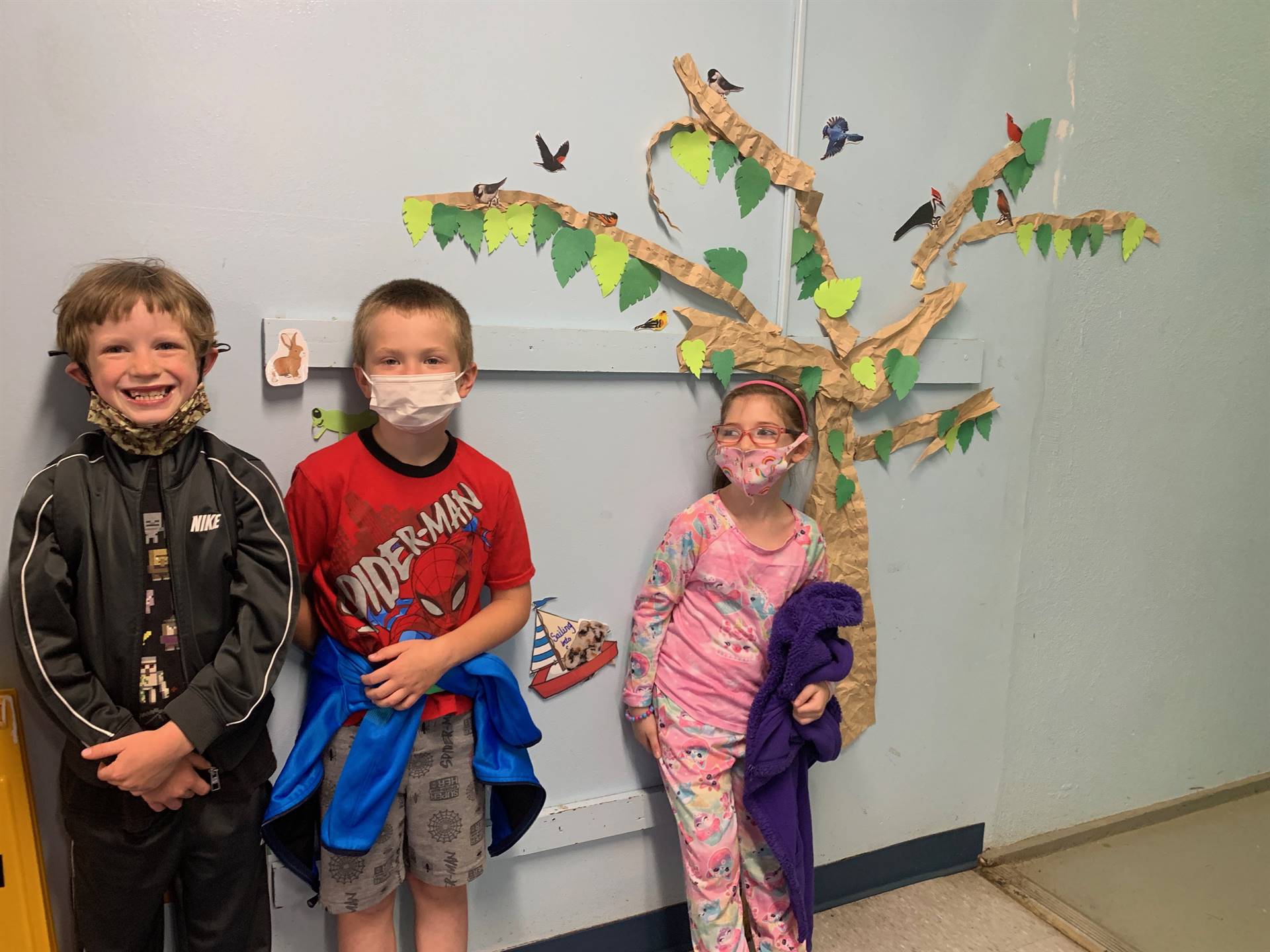 3 students stand. paper tree in background