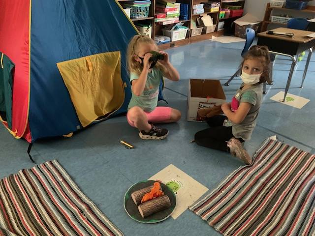 student sit by "fake" campfire and look through binoculars.