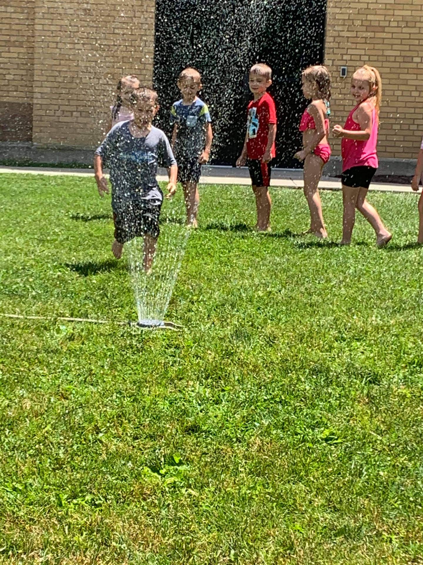 students running under sprinkler
