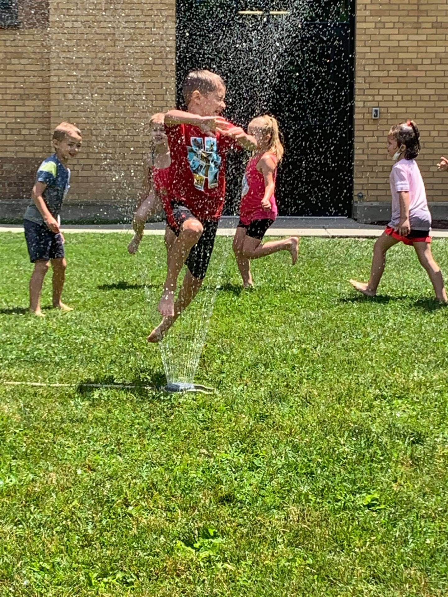 students running under sprinkler