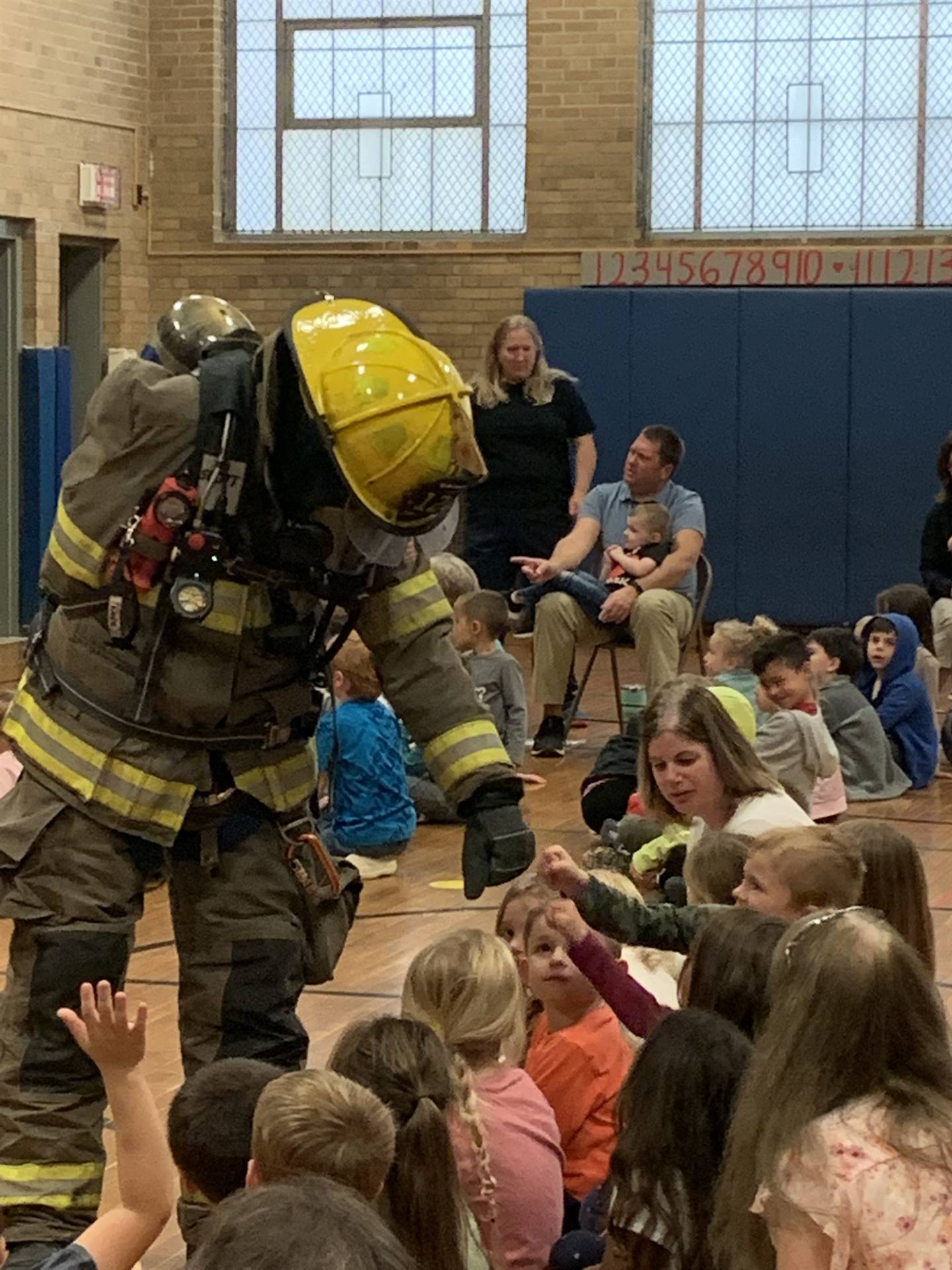 firefighters dressed in full gear and hats giving knuckle pounds to students