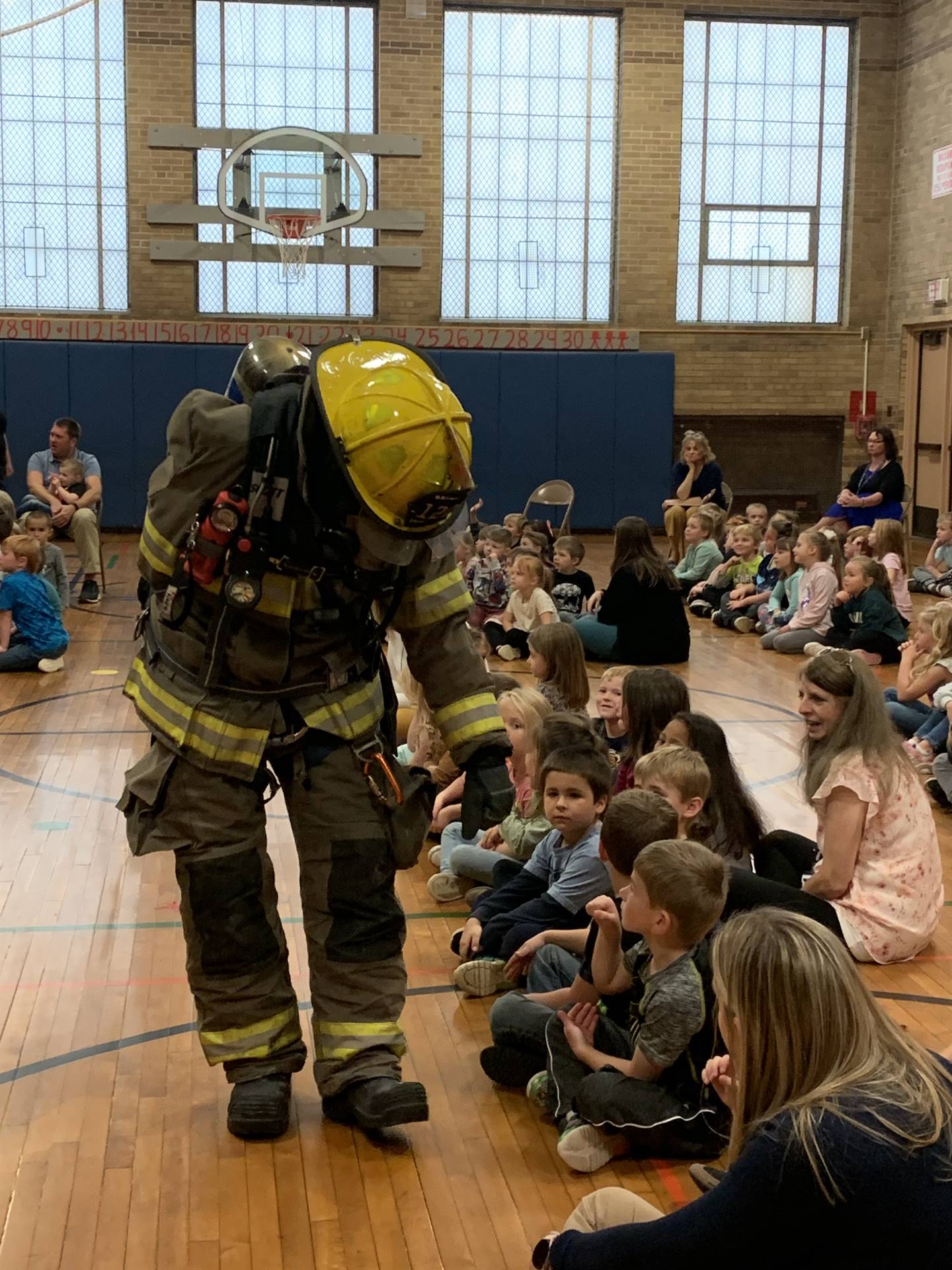 firefighters dressed in full gear and hats giving knuckle pounds to students