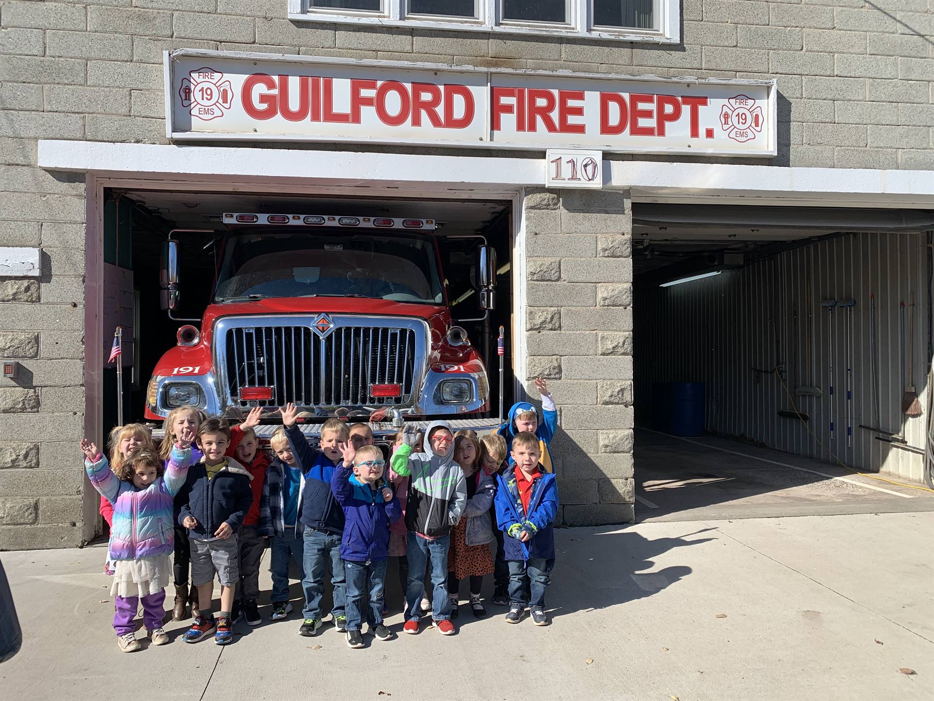 students standing in front a of a fire truck in a firehouse.