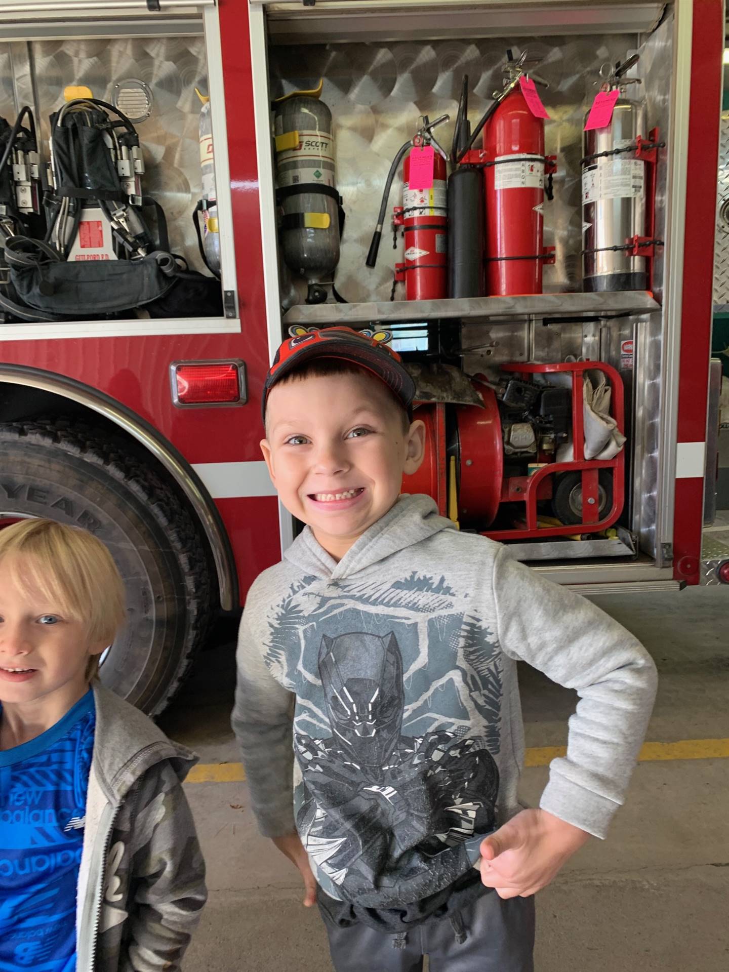 a boy with a big smile next to fire engine.