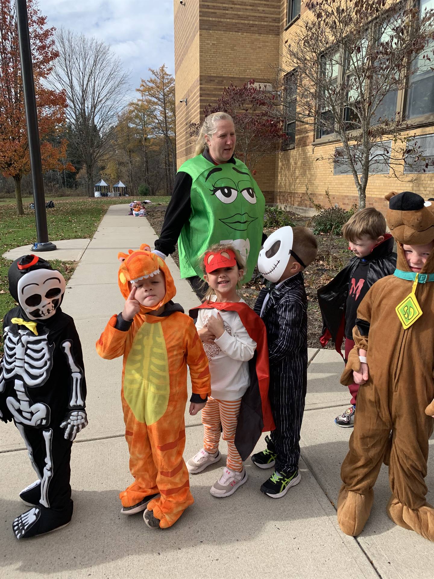a group of students in various halloween costumes with a teacher M&M behind them