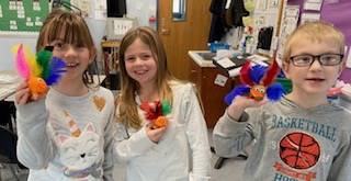 3 children holding a turkey craft with brightly colored feathers.
