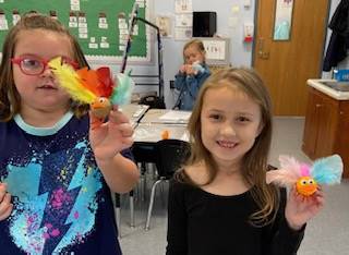 2 children holding a turkey craft with brightly colored feathers.