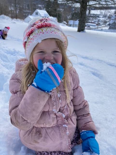 a student holds up a mittened hand to her face to lick snow