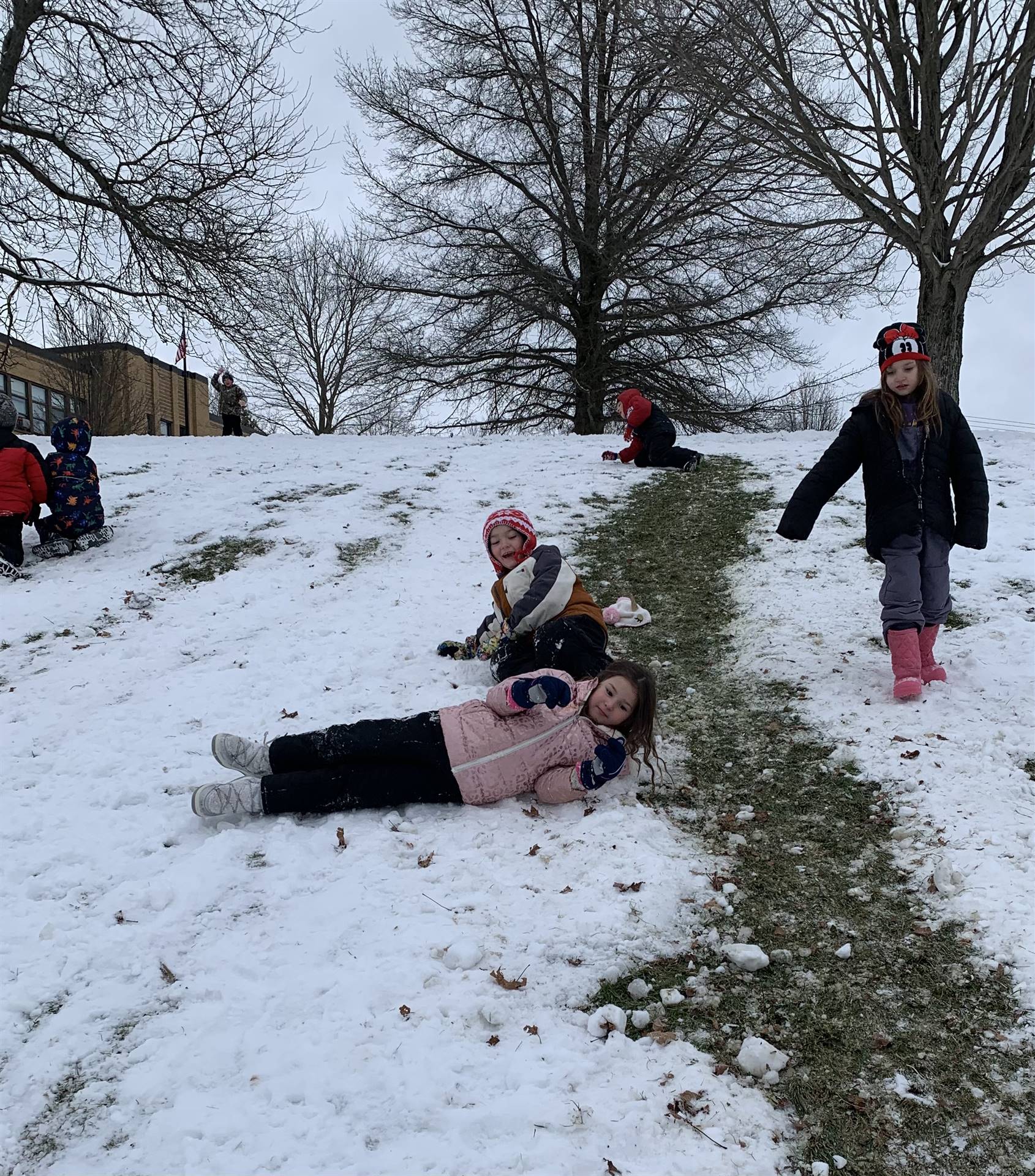 students rolling down snow-covered hill