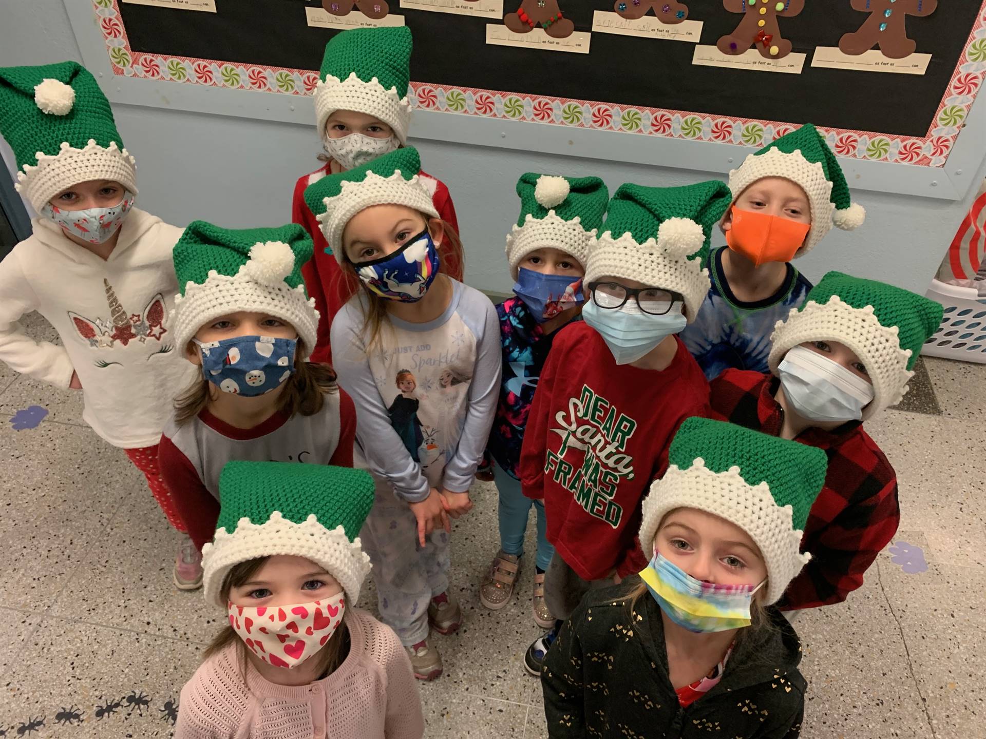 A group of students with green elf hats with white trim looking up. 