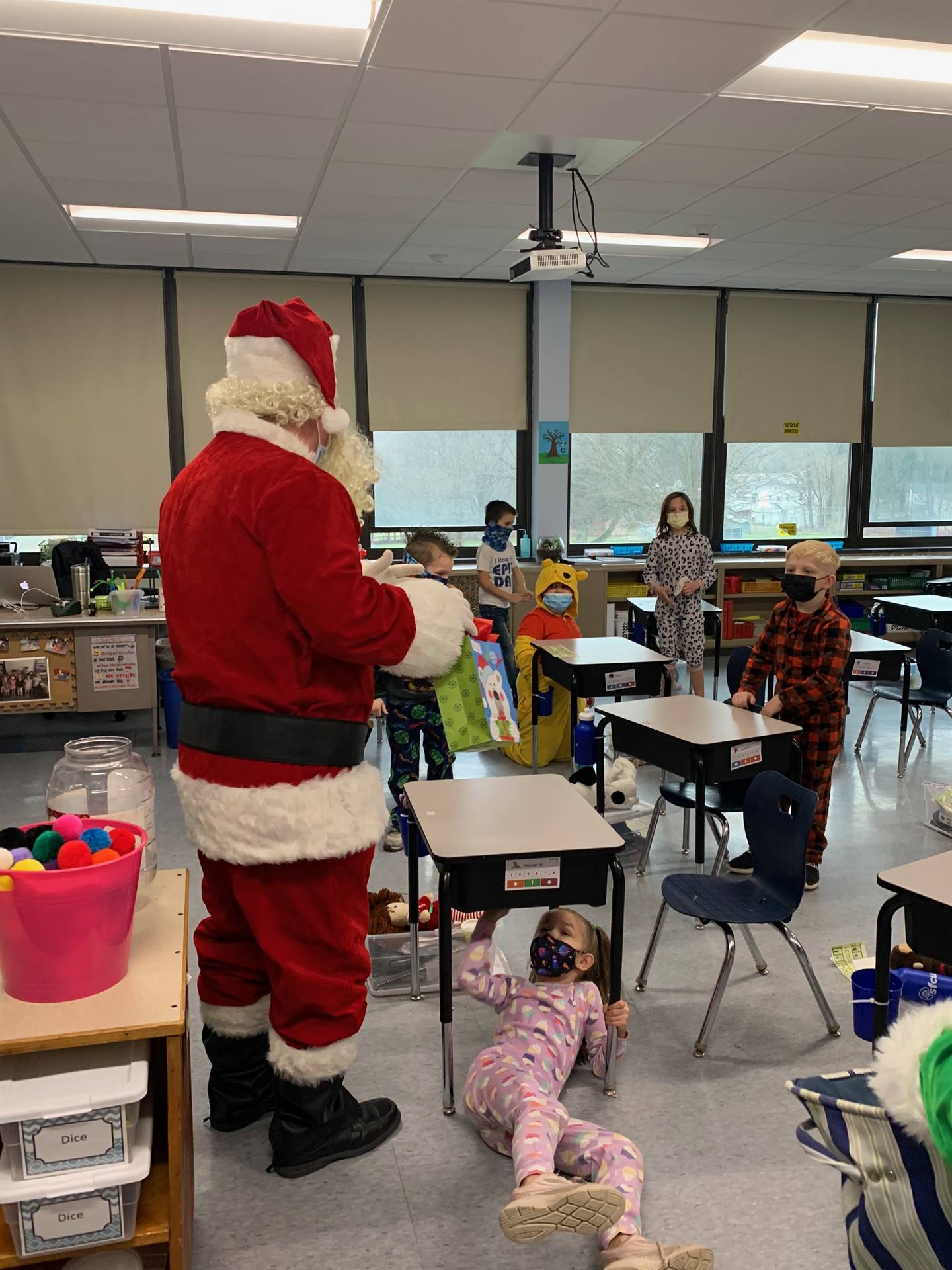 Santa talks with group of students and one student under a desk. 