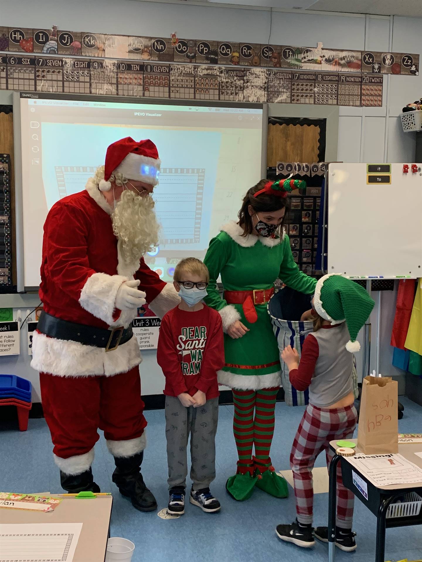 A student poses with Santa and elf while another student talks to Elf. 