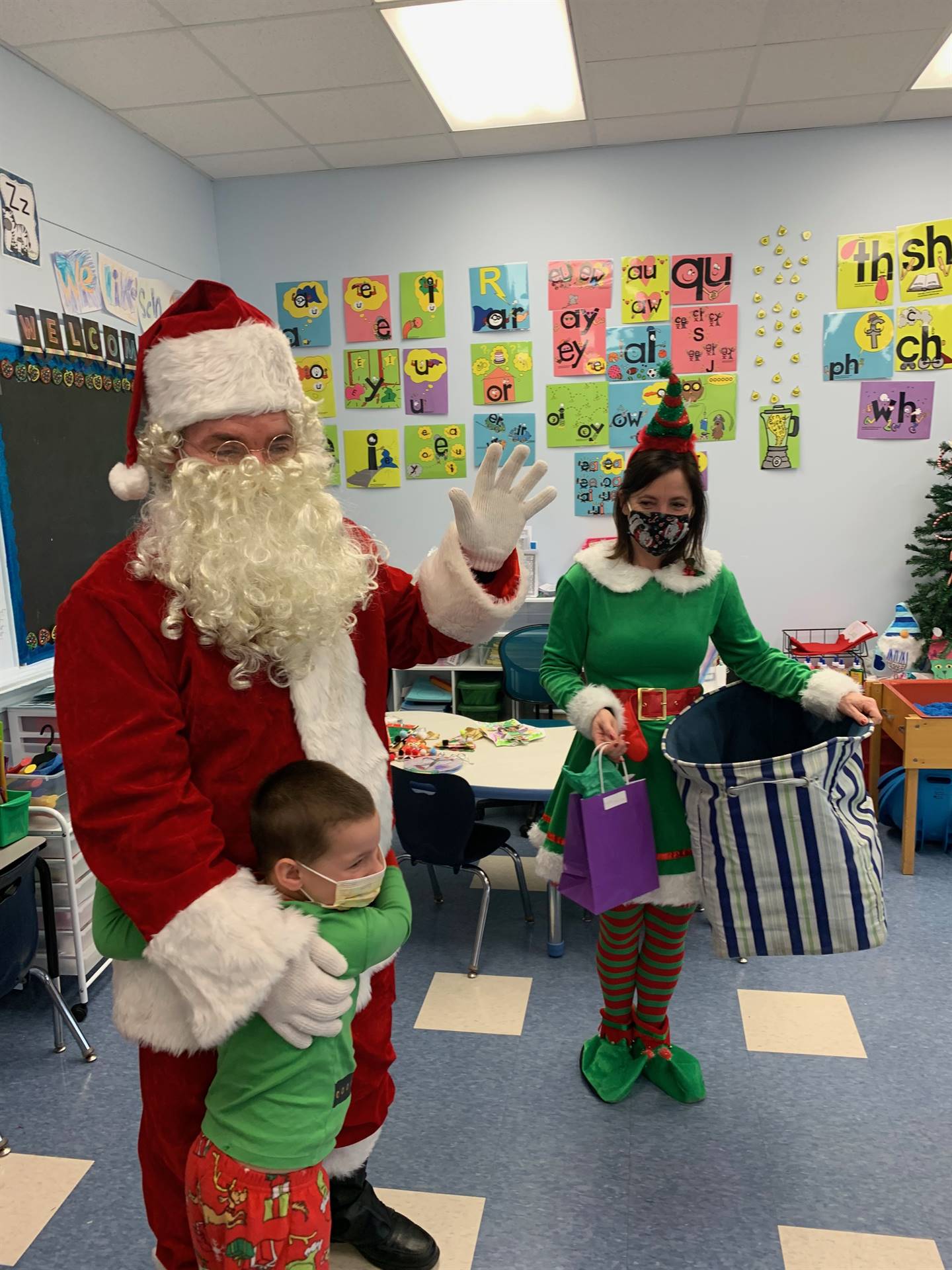 a student hugs Santa and elf stands by with huge sack bag. 