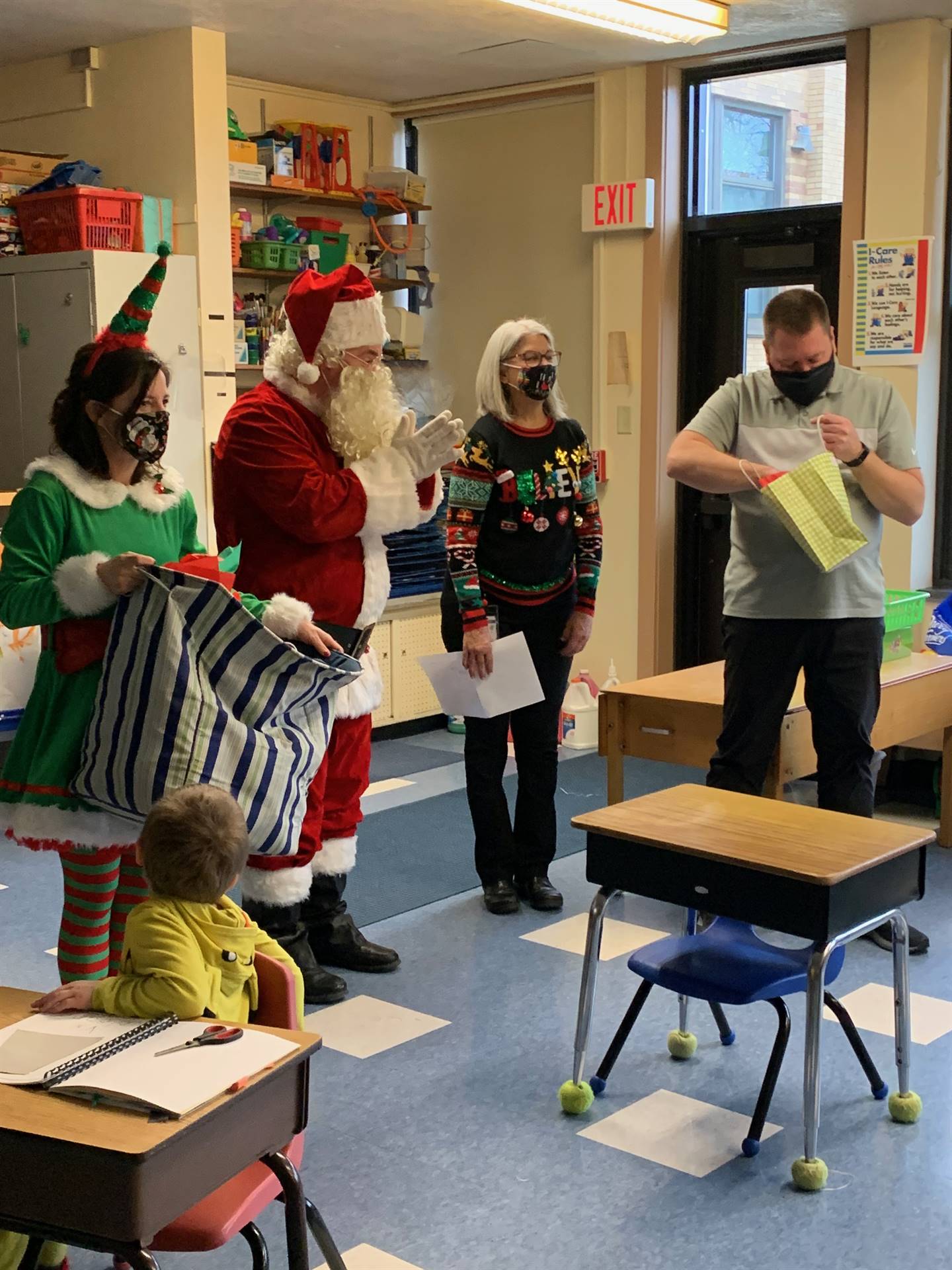 Santa enters classroom and hands bag to teacher. 