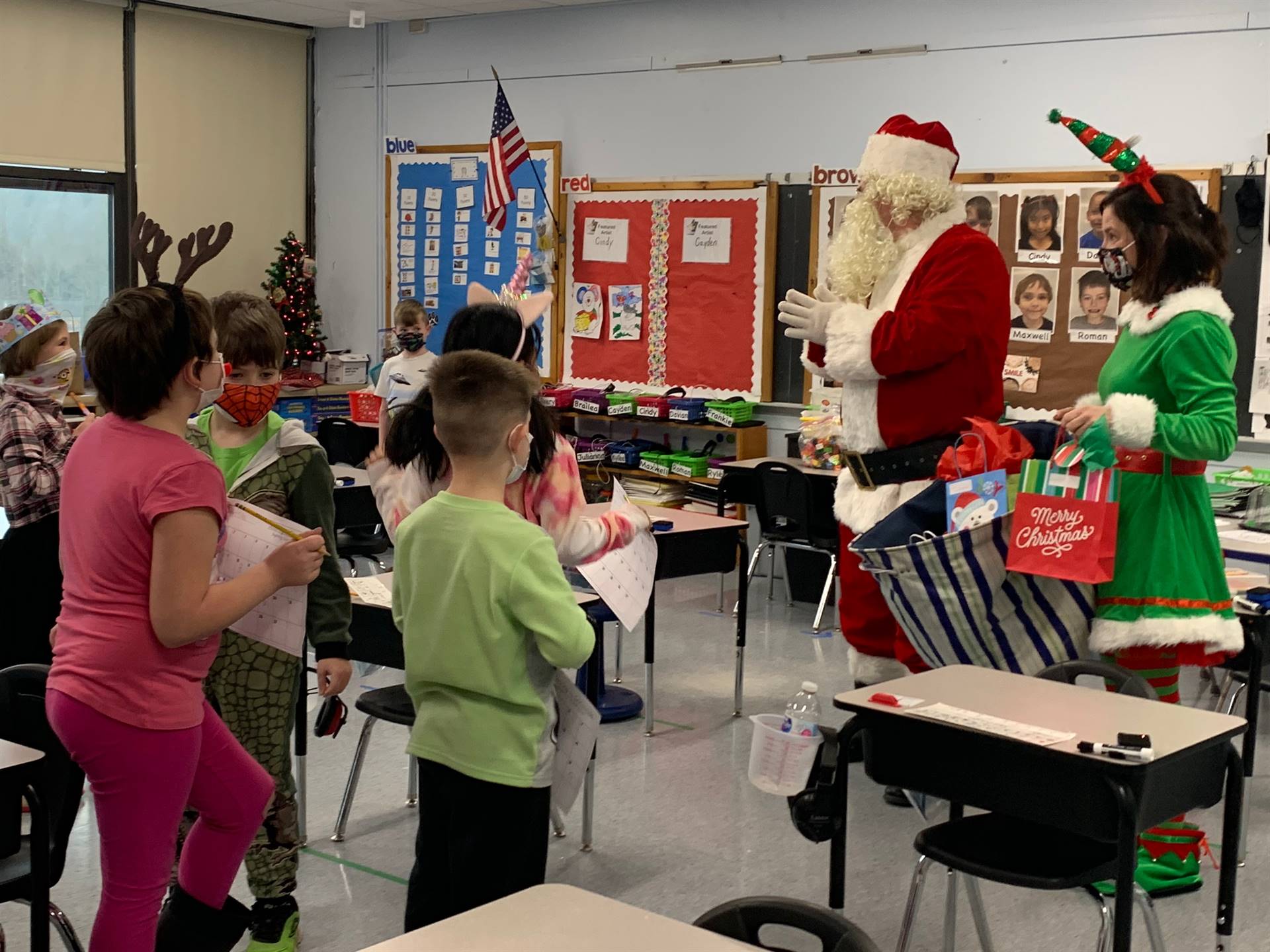 Santa talks with group of students wearing reindeer antlers. 