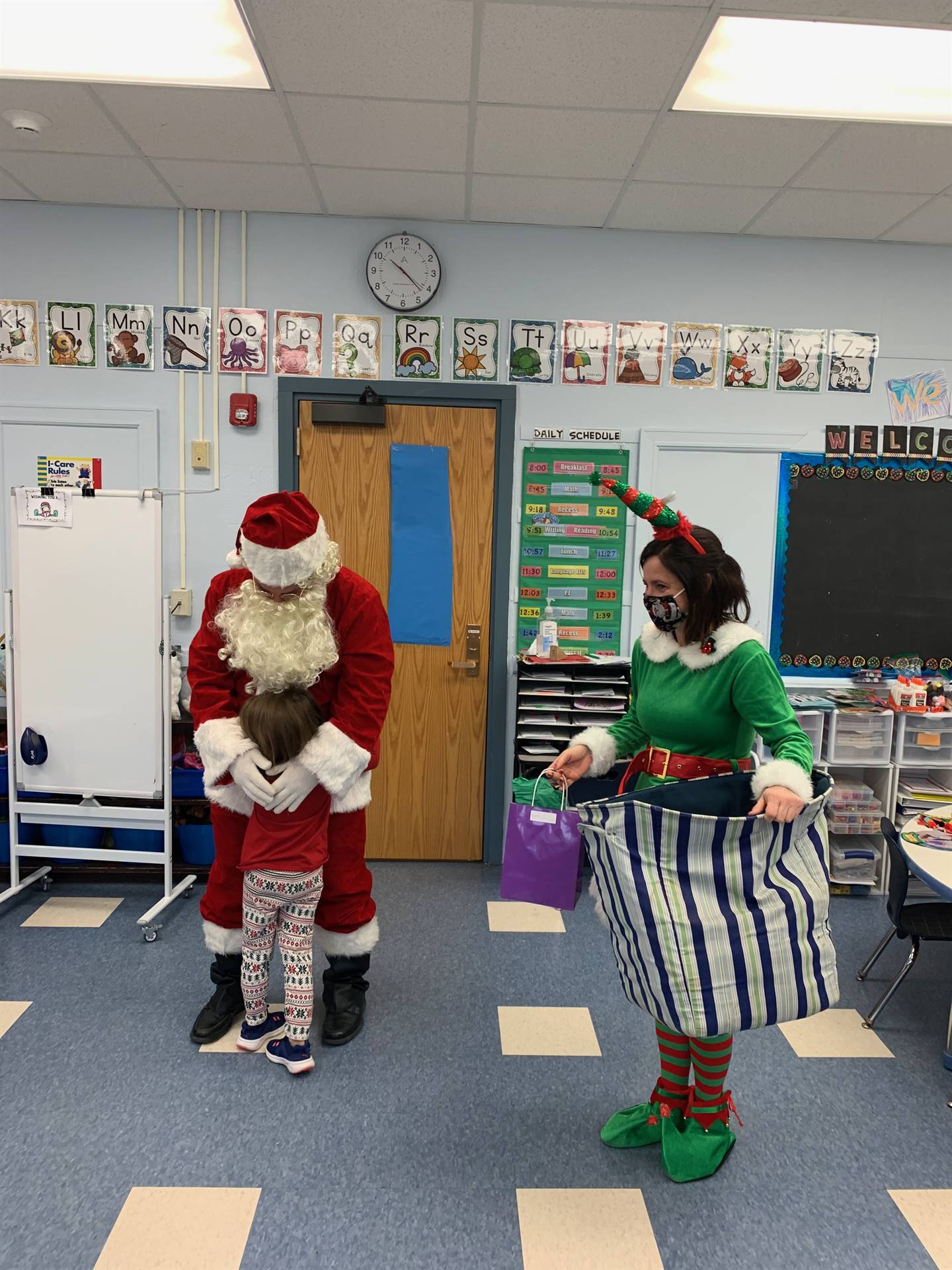 a student hugs Santa with Elf standing by.