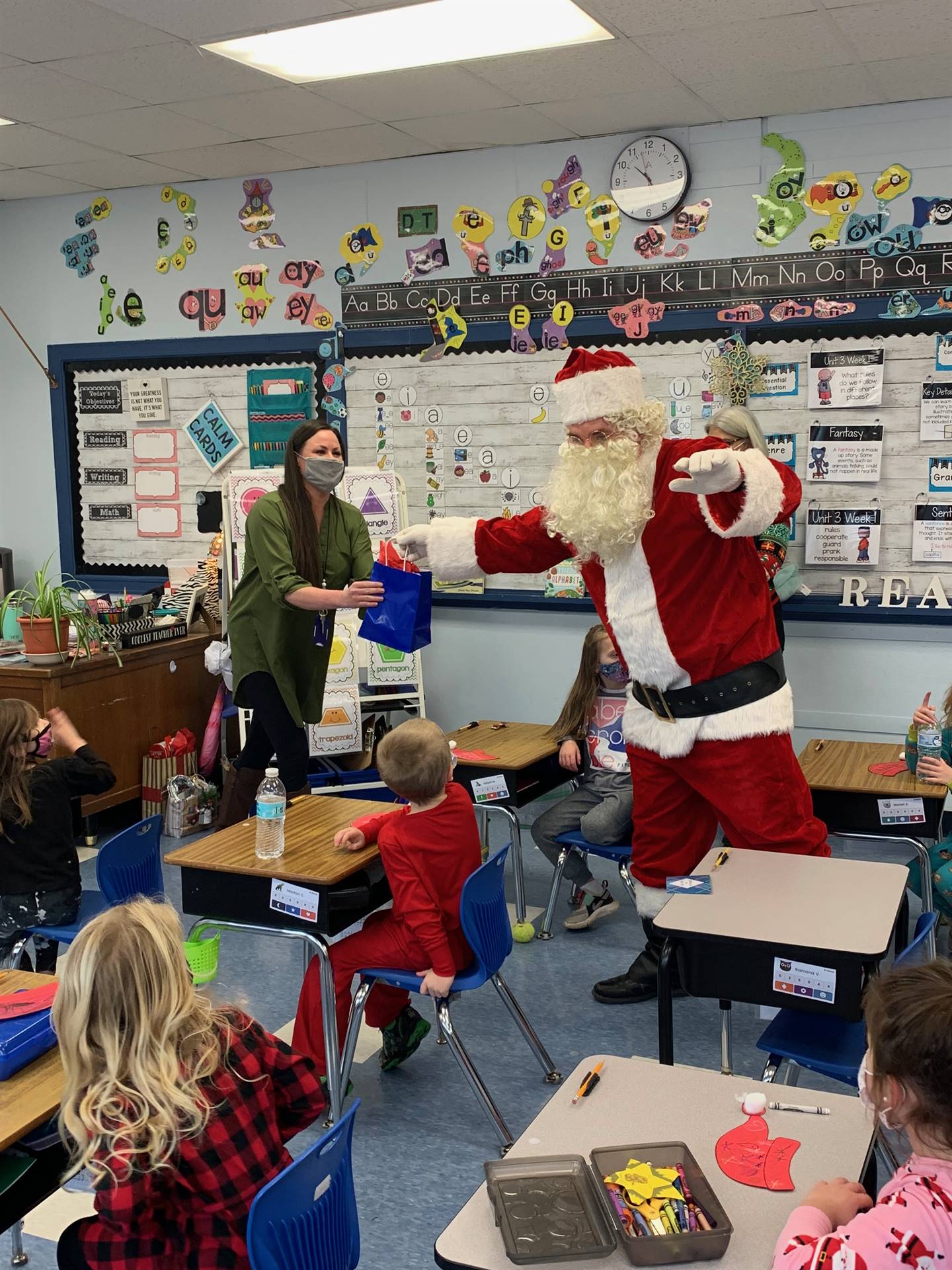 Santa is waving both hands and talking with students. 