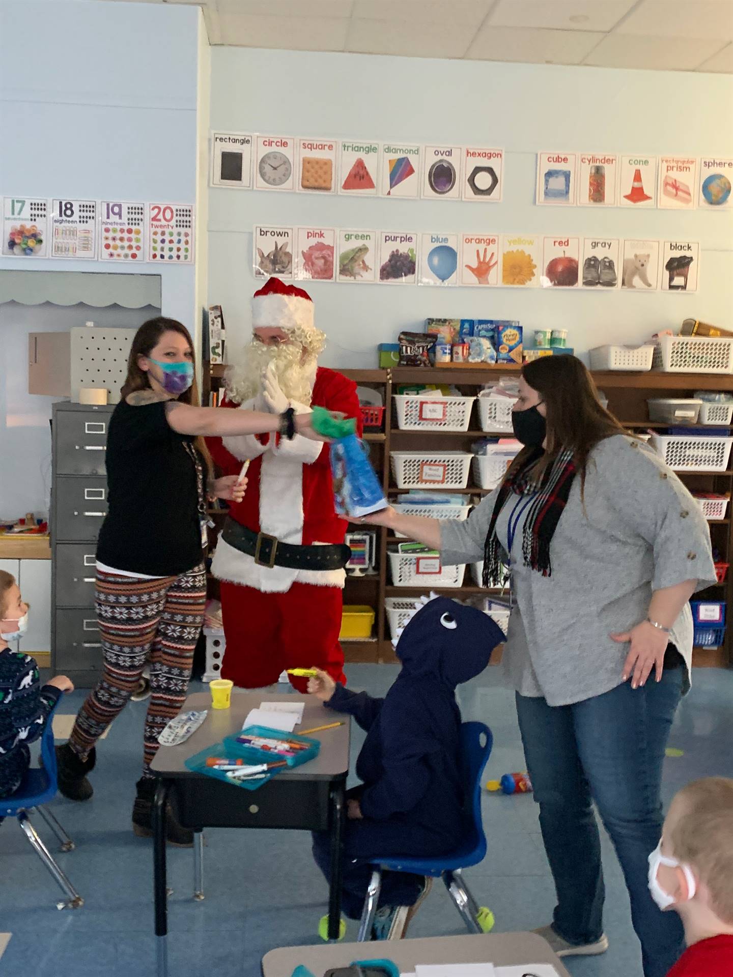 adult takes bag from santa and hands to teacher. 