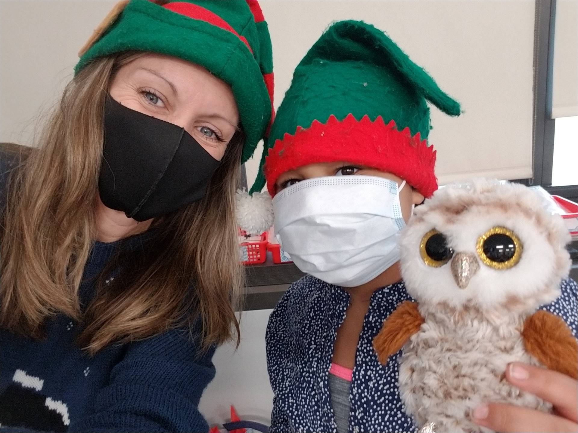 a teacher and student with elf hats on and student holding a stuffed owl.