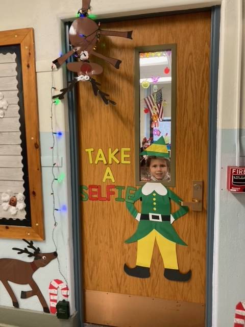 student peeks head through door window to that is decorated as an elf. 