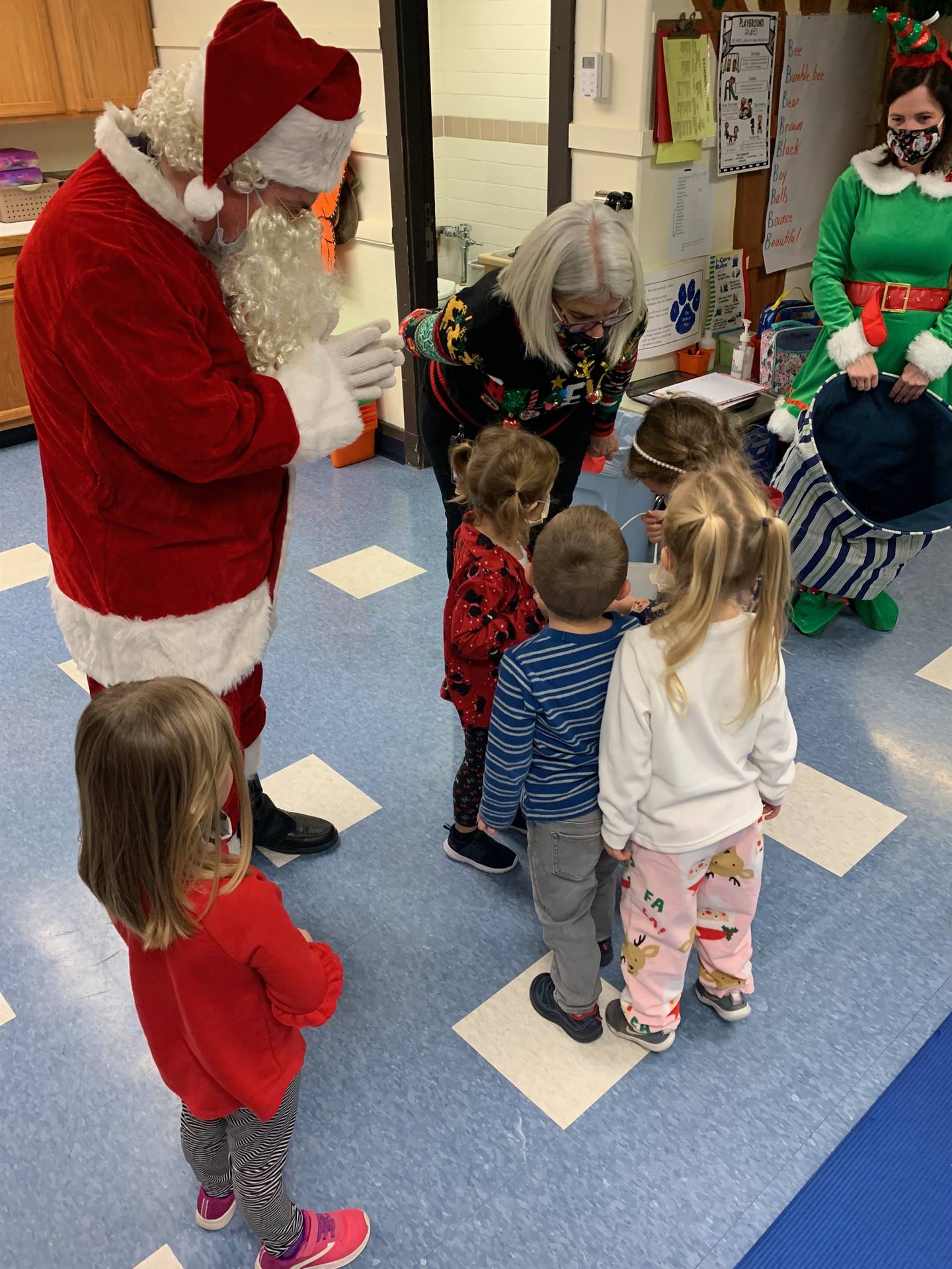 Santa is talking with 4 small children while principal listens to children.