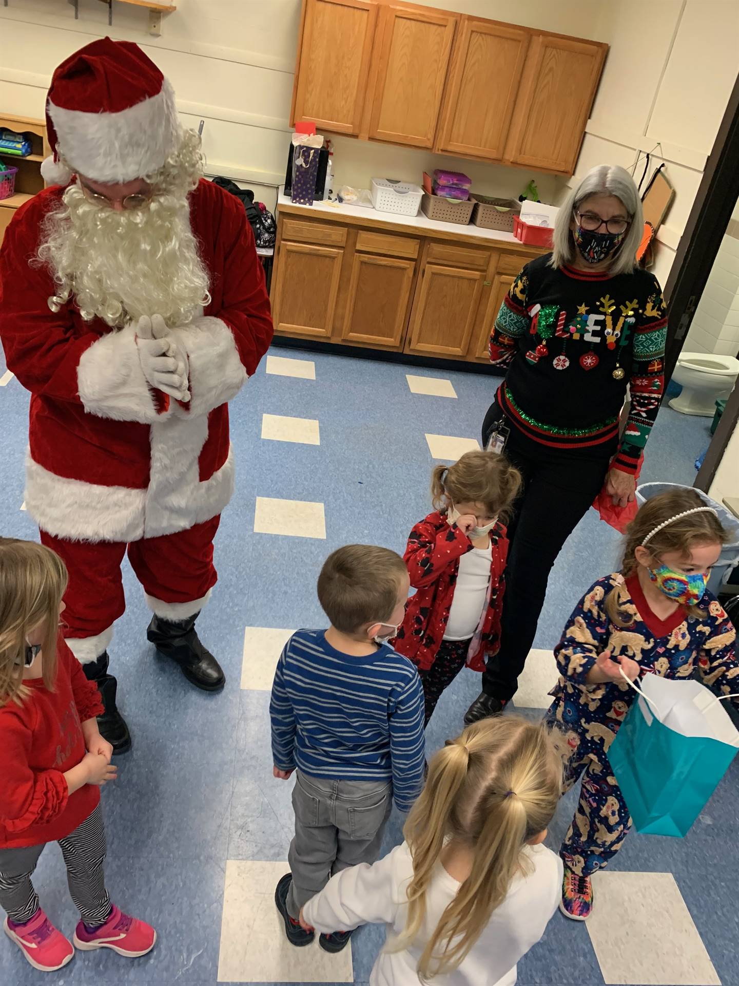 Santa is talking with 4 small children while principal listens to children.