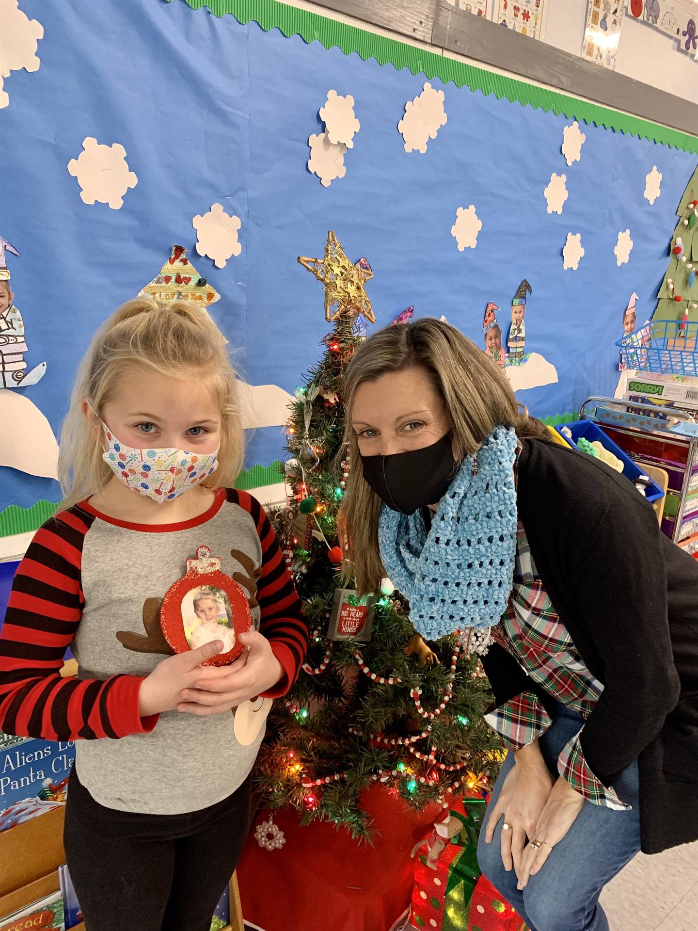 A teacher with blue scarf stands with student holding an ornament. blue background. 