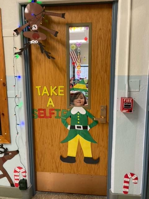 student peeks head through door window to that is decorated as an elf. 