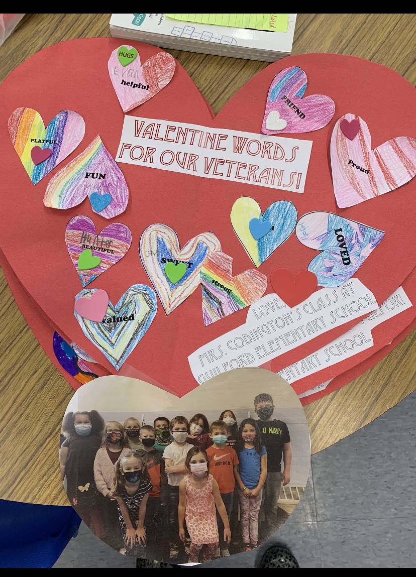 A large paper red heart with multicolored hearts glued on and a class picture attached to bottom