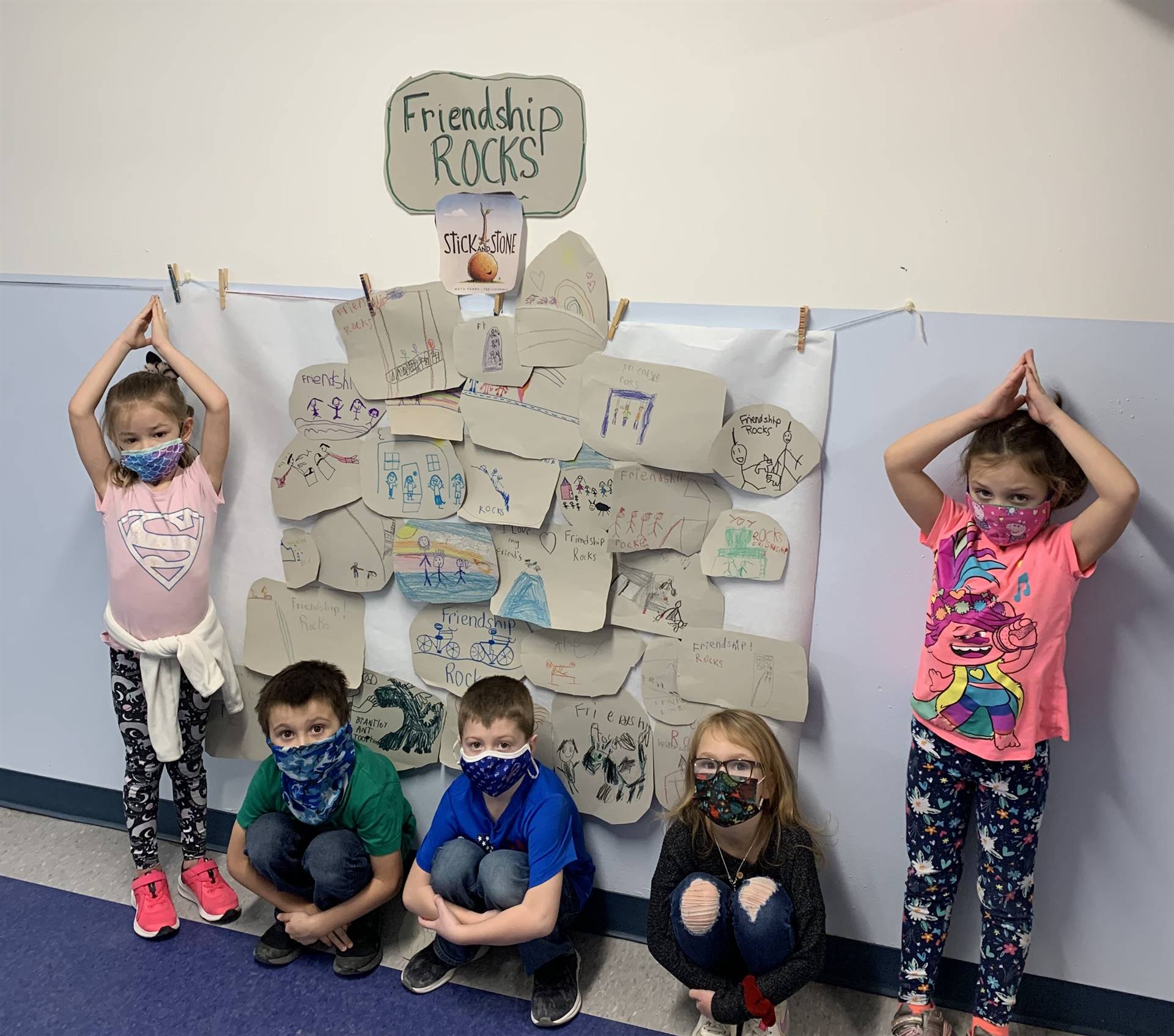 STUDENTS in front of wall covered in paper gray rocks and sign saying "Friendship Rocks"