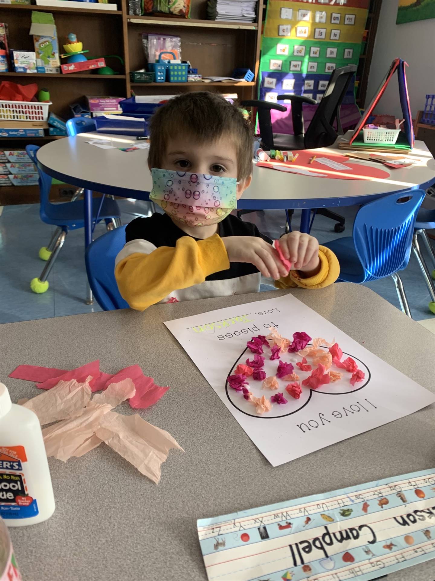 a student sitting at desk with completed heart covered in pink tissue paper.