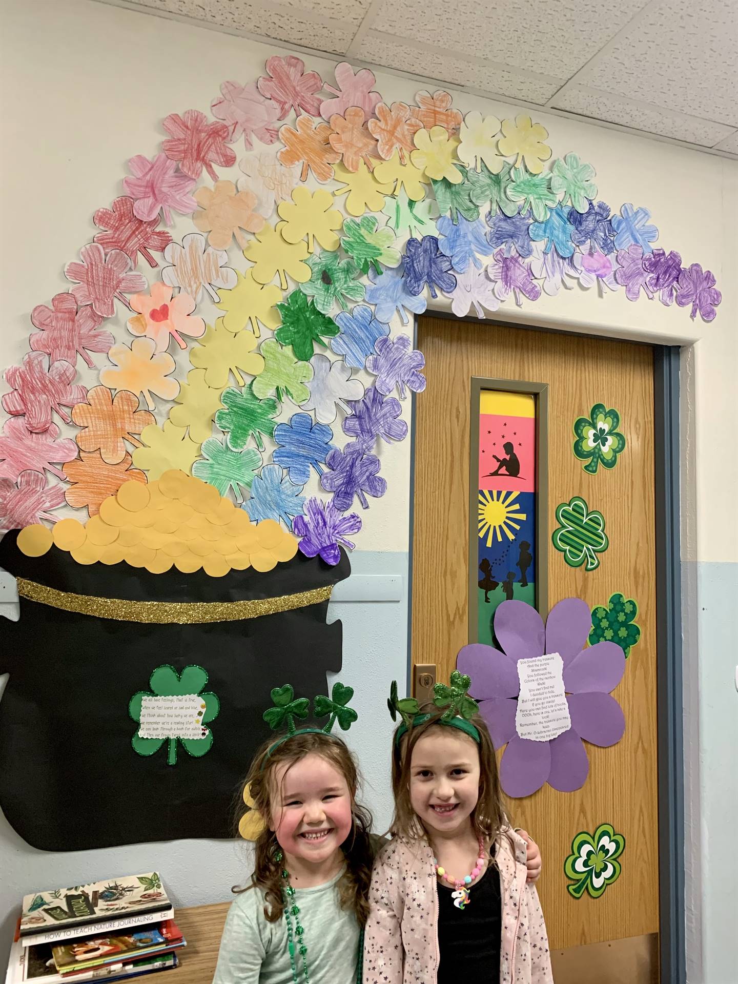 2 students with green shamrock headbands and a pot of gold and rainbow behind them