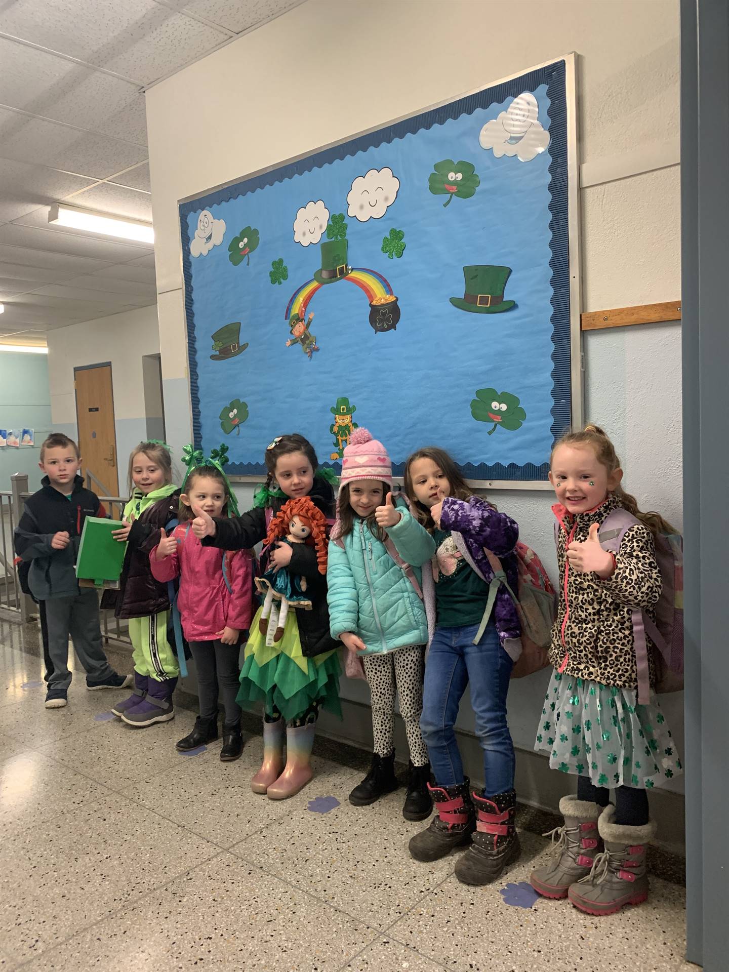 a group of students with a bulletin board covered in blue with green hats, shamrocks and a rainbow b