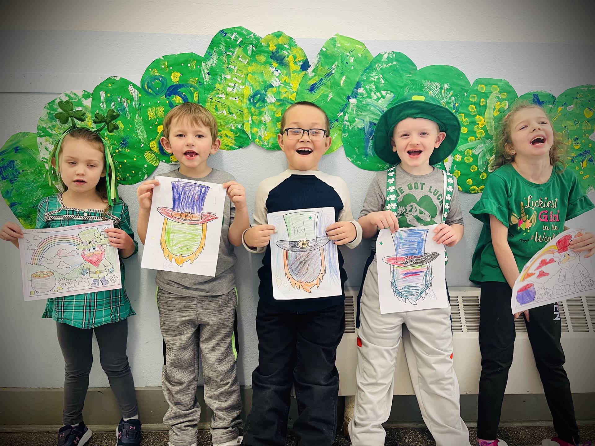 5 students hold leprechaun faces colored against a background of a giant green caterpillar