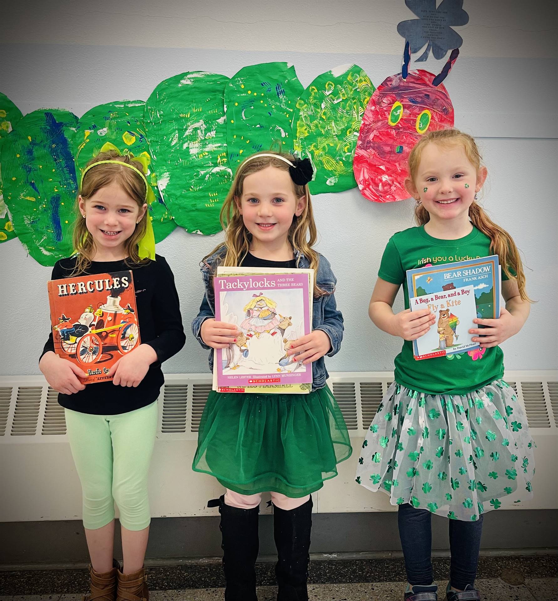 3 students with books and a giant green caterpillar background