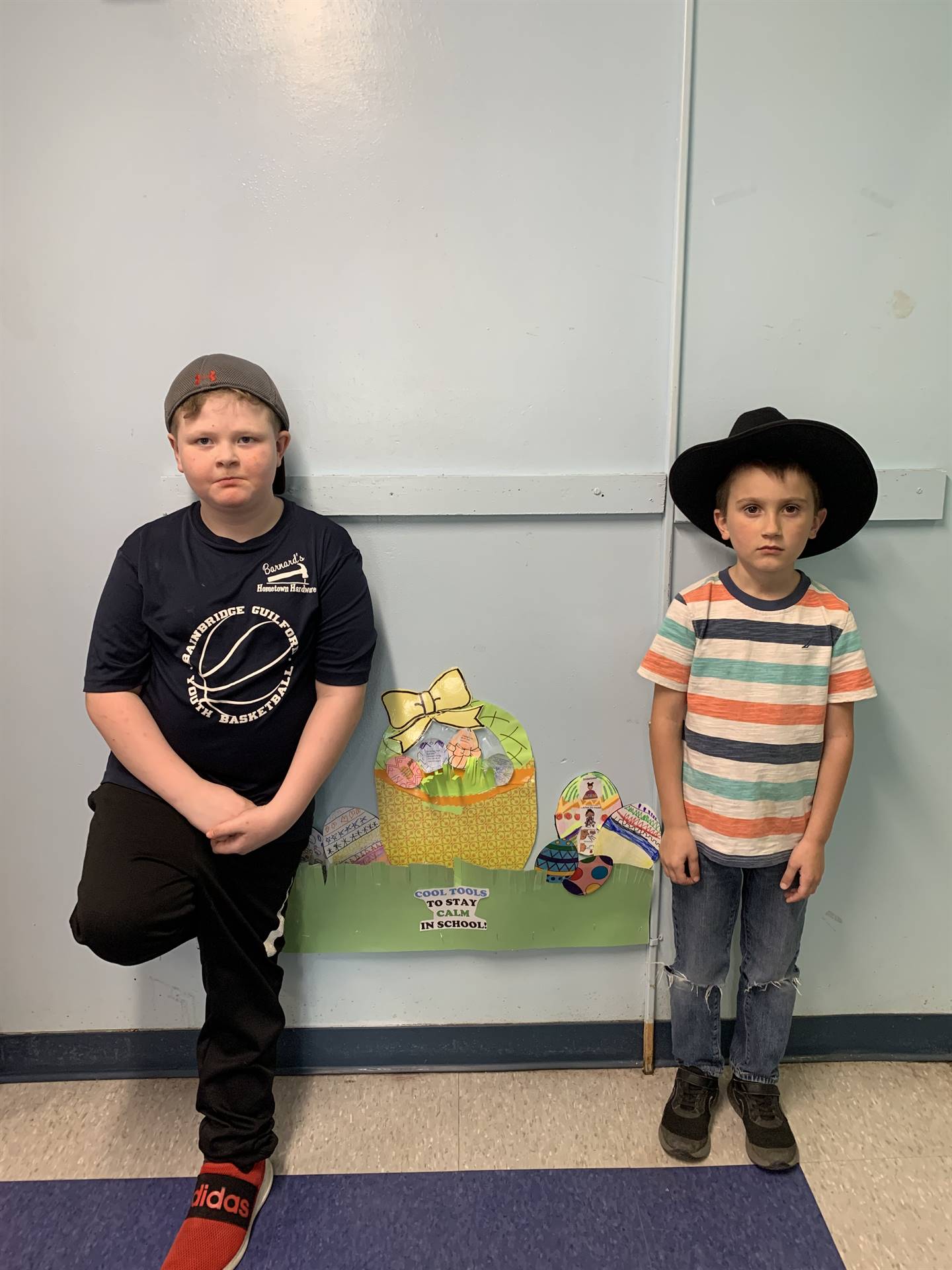 2 students against wall. 1 with wide brim hat and other with baseball cap.