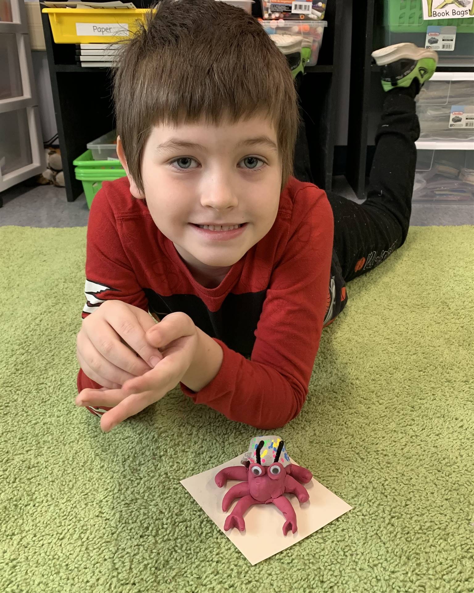 child laying on green carpet with red clay crab.