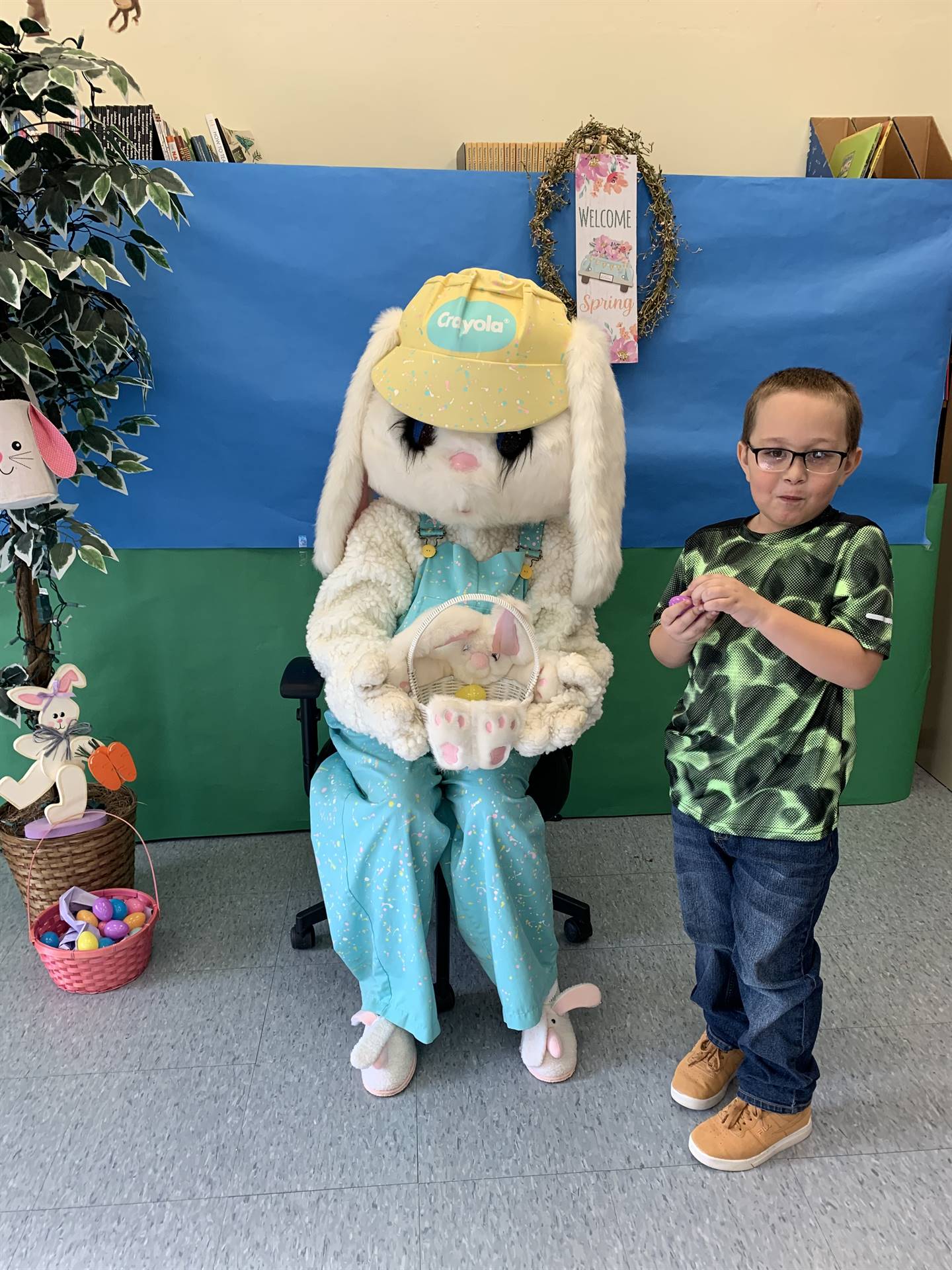 a boy standing next to an adult dress up bunny with green and blue back drop