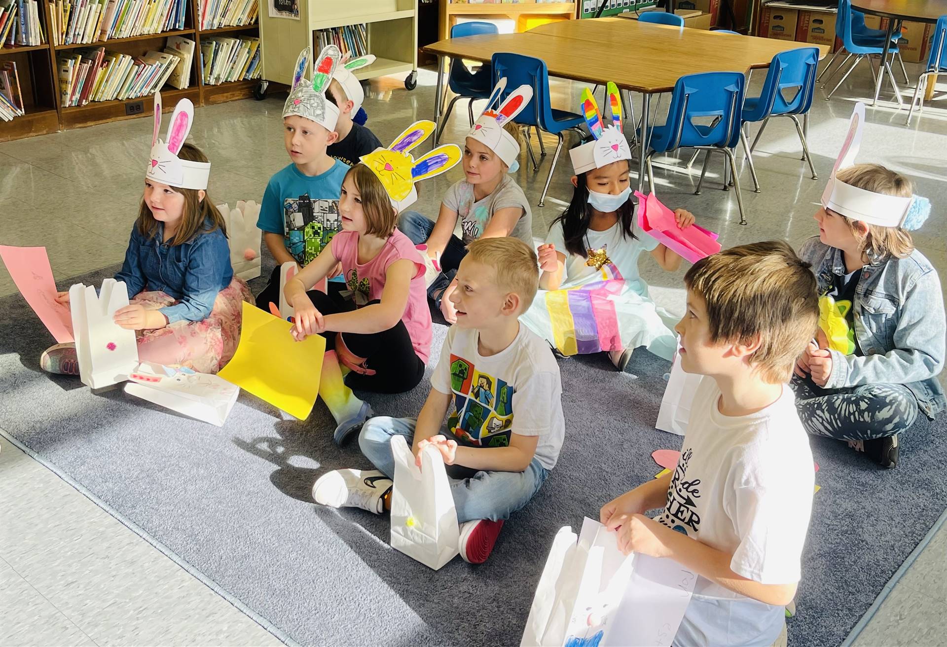 a group of students holding white paper bunny bags seated on floor