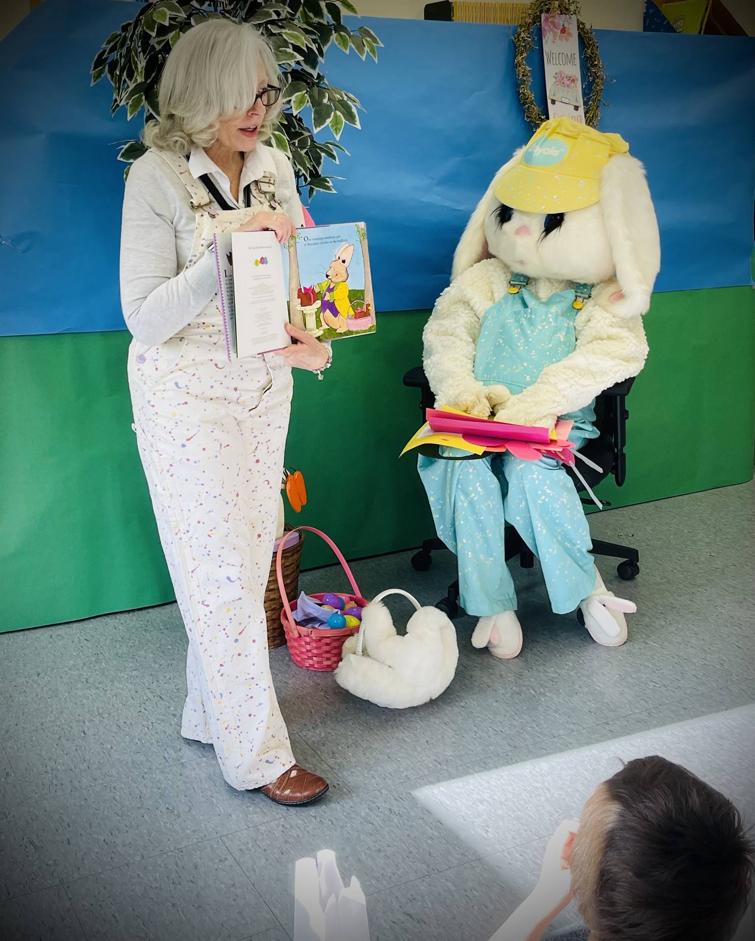 An adult reading a spring story while an adult dressed as a spring Bunny  looks and listens