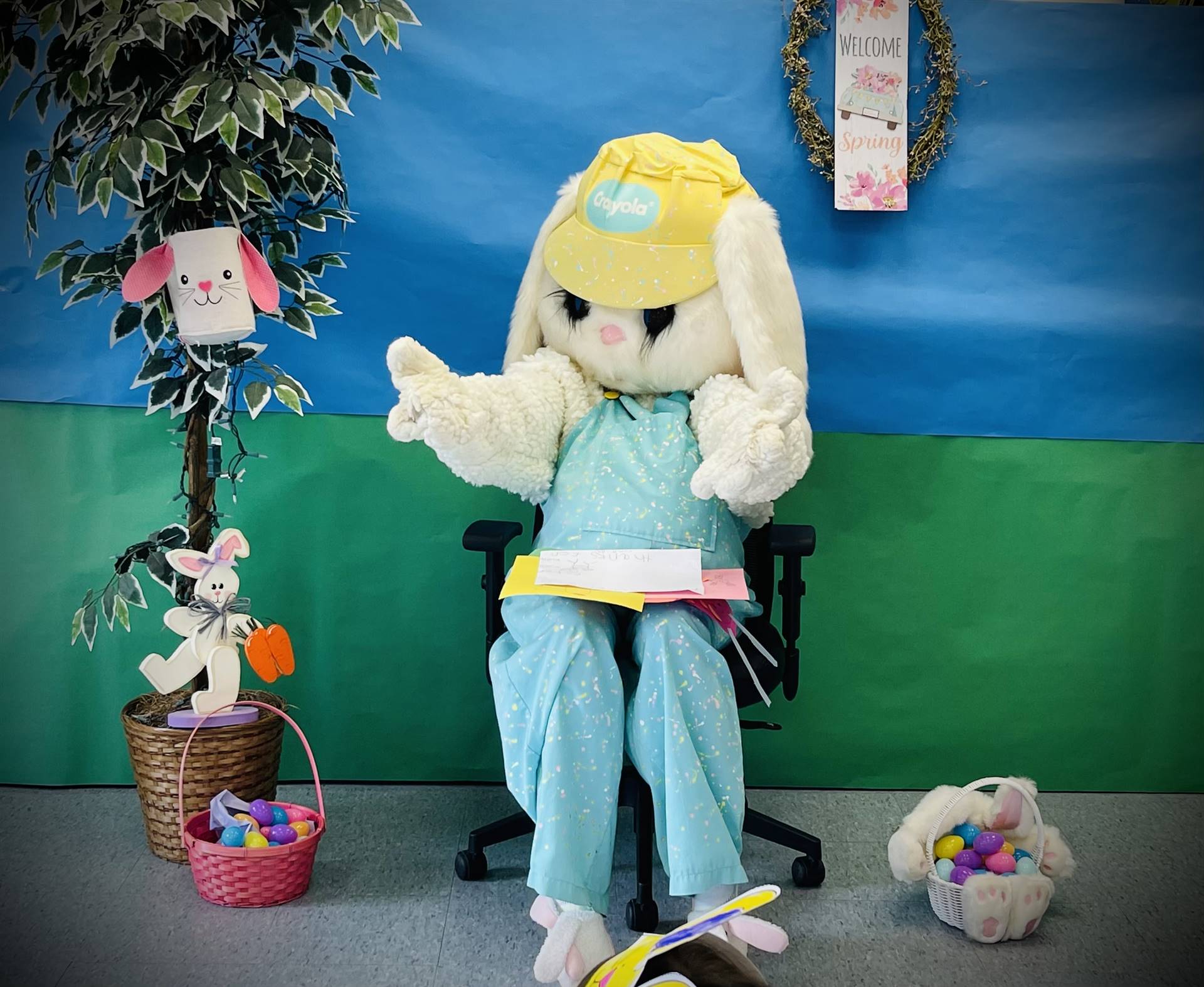 Adult dressed as a spring bunny sits on chair with blue and green background.