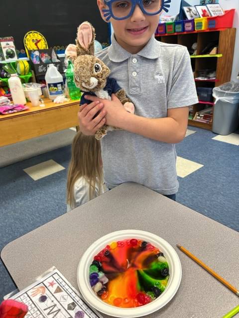 student holding stuffed bunny by a plate with rainbow colors.