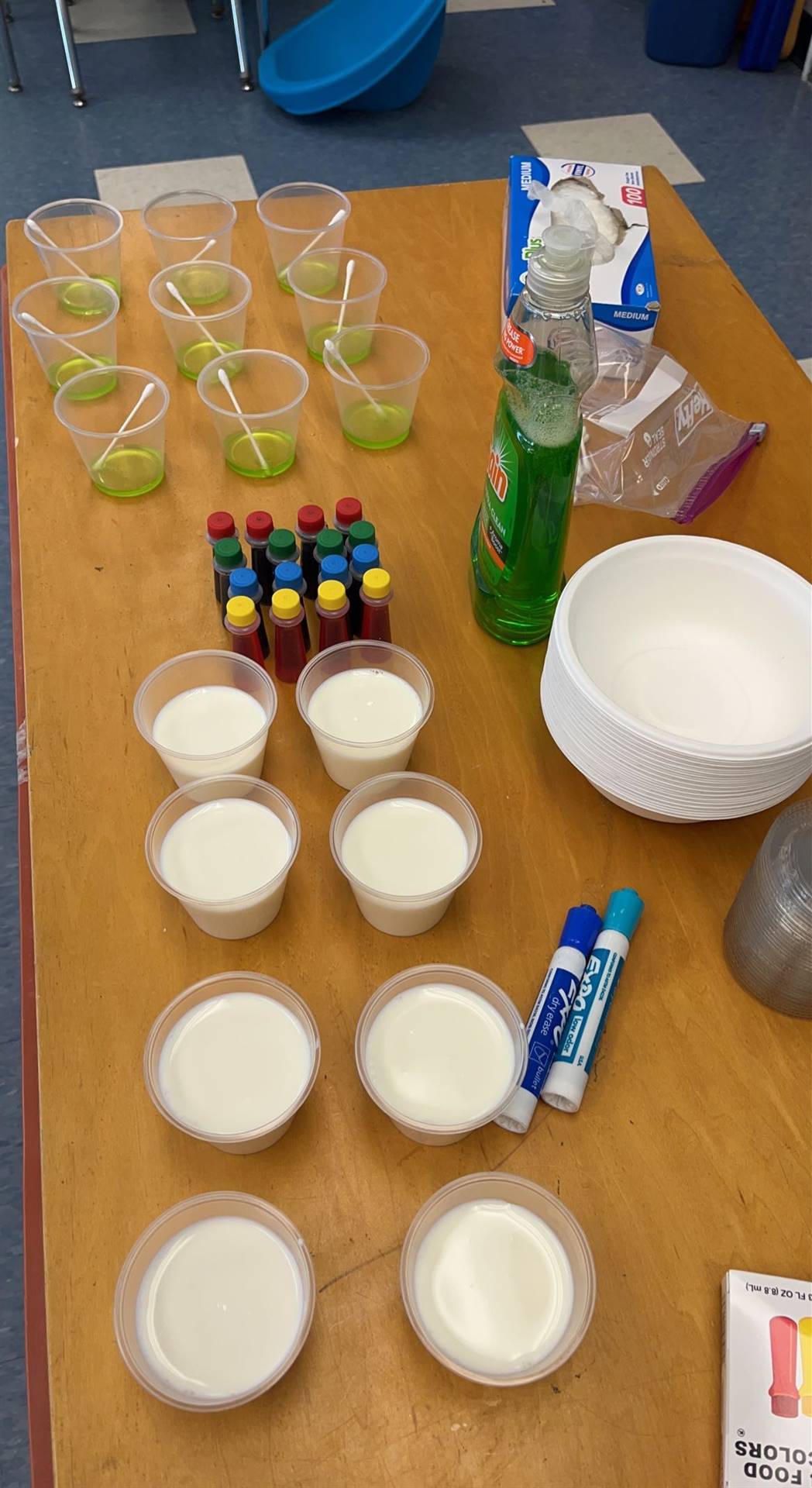 table with cups of glue, food coloring and other supplies for a science experiment