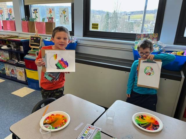 2 students hold up a colored rainbow and a plate of skittles melted into a rainbow