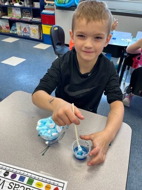 A student dipping into blue liquid sitting at his desk.