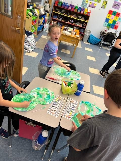 3 students sitting at desks with green and blue art supplies 