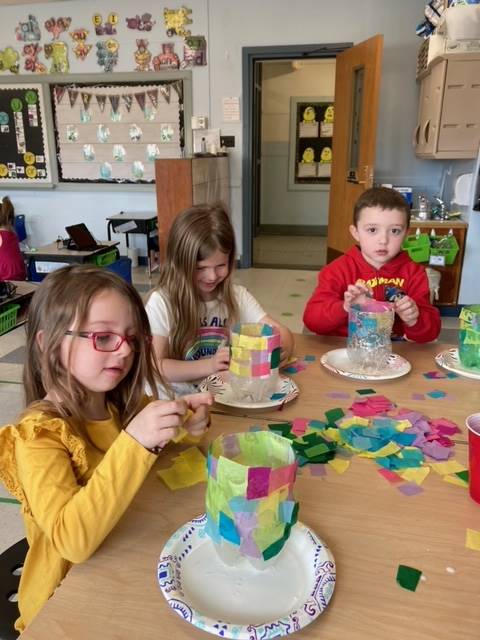 students gluing on colored paper to plastic bowl.