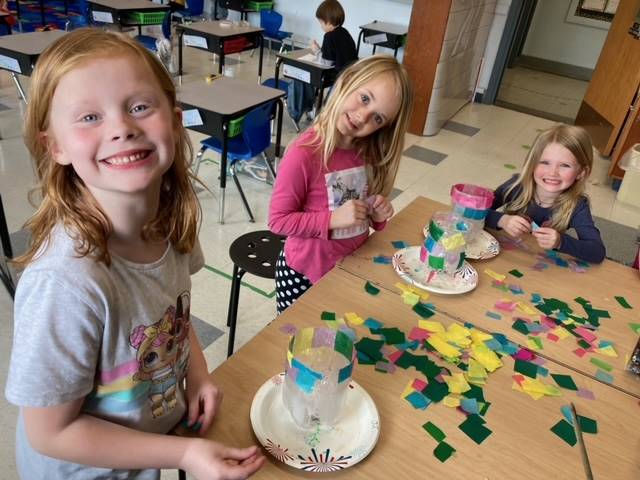 students gluing on colored paper to plastic bowl.