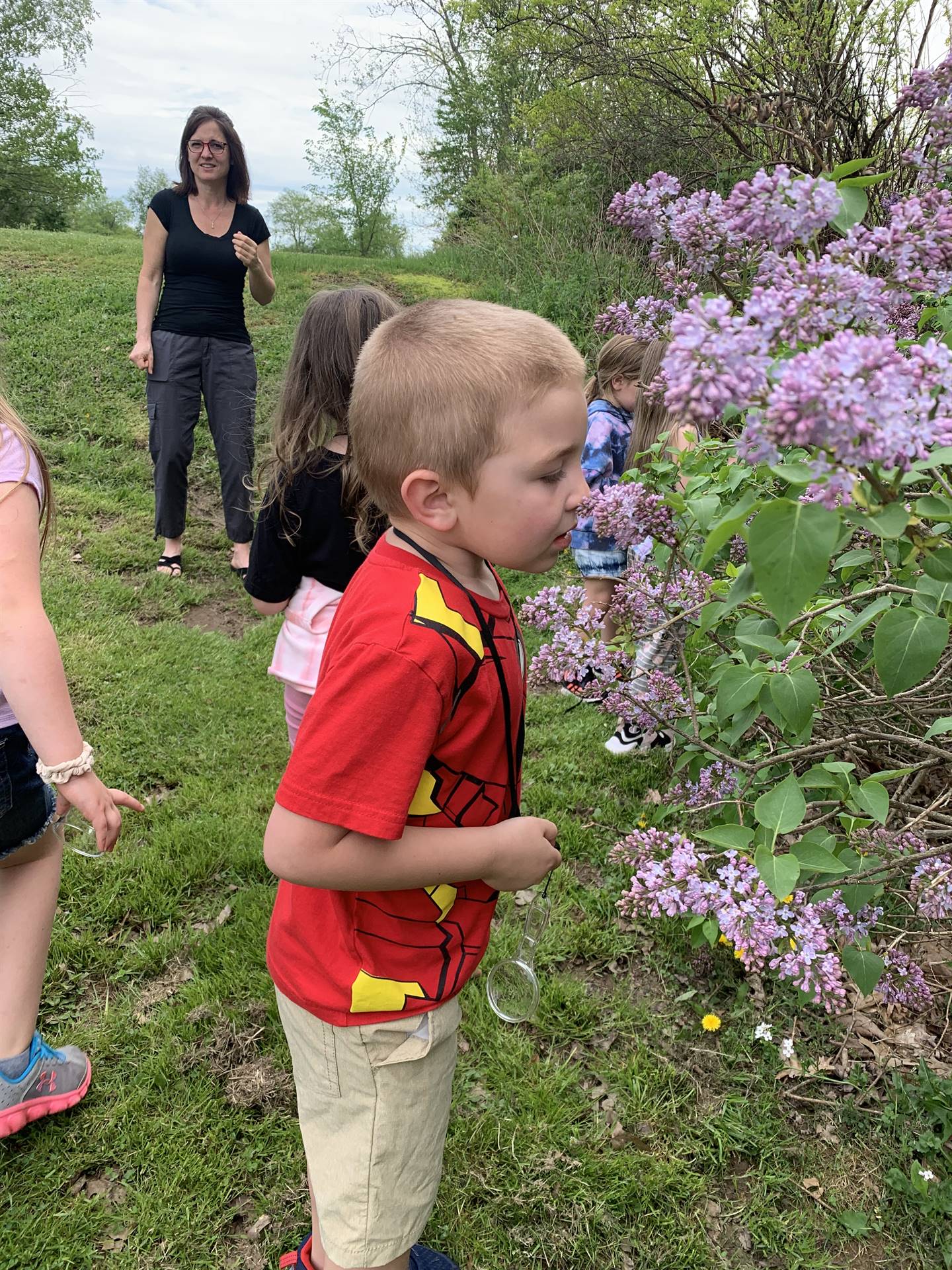 child smelling lilacs while adult watches